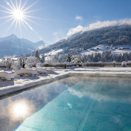 Winterlicher Pool vor verschneiter Berglandschaft im Sonnenschein