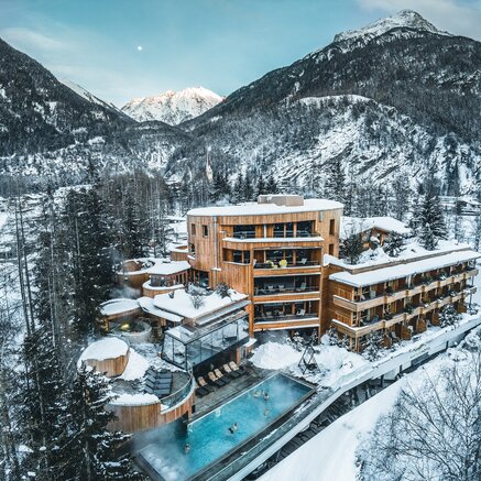 Hotel Waldklause im Winter vor schneebedeckten Bergen mit Pool und Holzbauten